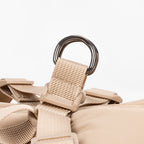 Close-up detail of beige padded harness vest showing metal D-ring attachment and nylon straps.