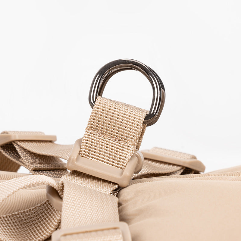 Close-up detail of beige padded harness vest showing metal D-ring attachment and nylon straps.
